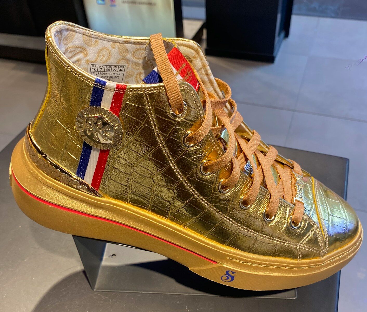 A golden sneaker with fancy embellishments is on display.